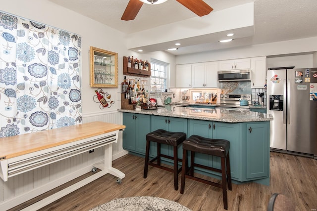 kitchen with light stone countertops, appliances with stainless steel finishes, dark hardwood / wood-style floors, and white cabinets