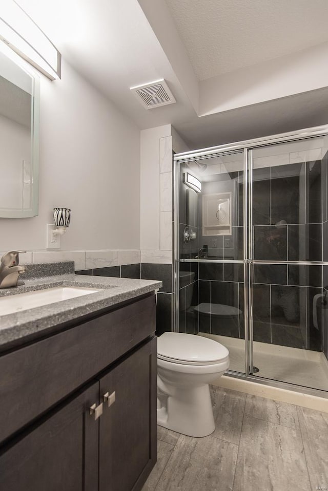 bathroom featuring vanity, toilet, a shower with shower door, and tile walls