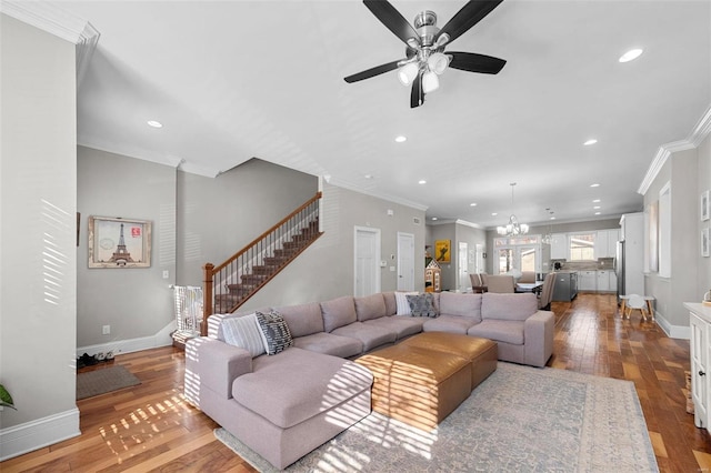 living room with crown molding, ceiling fan with notable chandelier, and light wood-type flooring