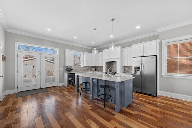 kitchen featuring stainless steel fridge, a breakfast bar area, white cabinets, and a center island with sink