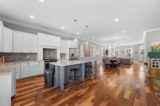 kitchen with appliances with stainless steel finishes, a breakfast bar, pendant lighting, white cabinets, and a kitchen island with sink