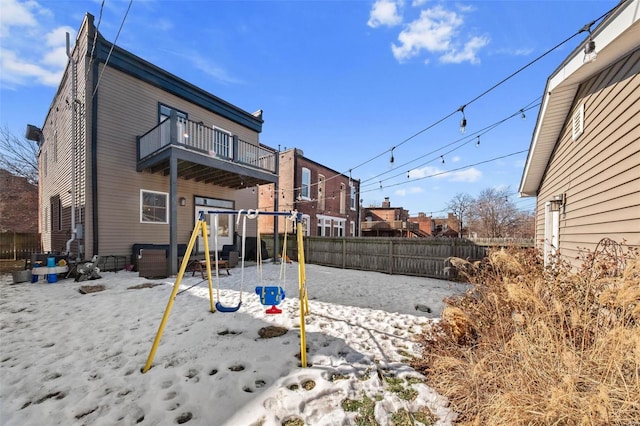 snow covered rear of property with a playground and a balcony