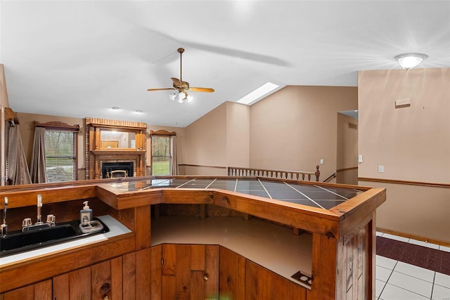 kitchen featuring lofted ceiling, sink, light tile patterned floors, ceiling fan, and a fireplace