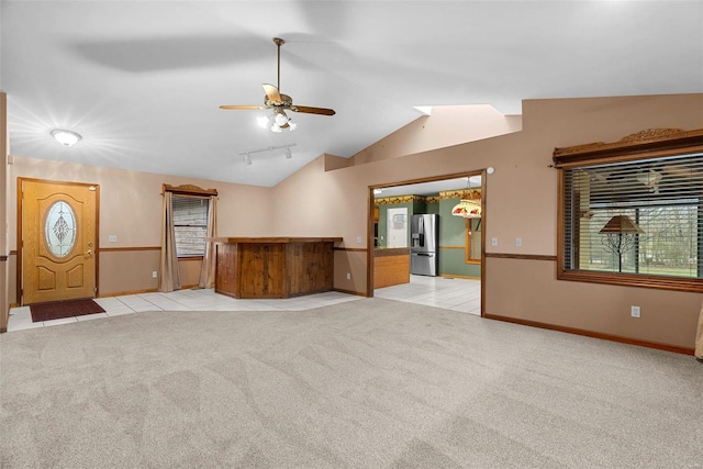 unfurnished living room with vaulted ceiling, rail lighting, light colored carpet, and ceiling fan