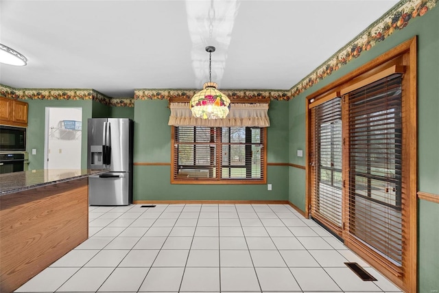 kitchen featuring light tile patterned flooring, dark stone countertops, hanging light fixtures, and black appliances