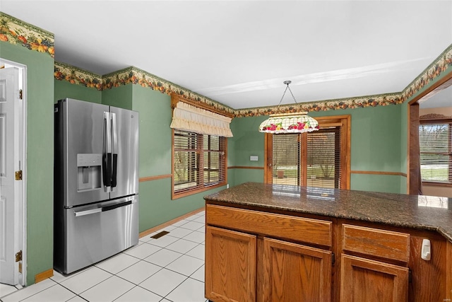 kitchen featuring dark stone countertops, light tile patterned floors, decorative light fixtures, and stainless steel fridge