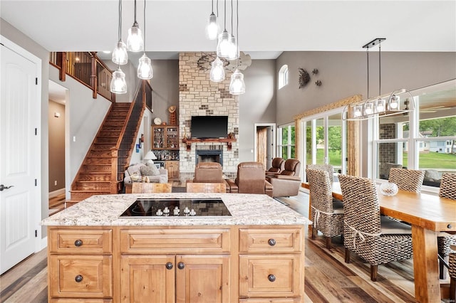 kitchen featuring light stone counters, a brick fireplace, light hardwood / wood-style flooring, pendant lighting, and black electric stovetop