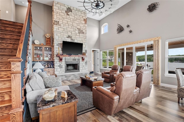 living room with a stone fireplace, a high ceiling, and light wood-type flooring