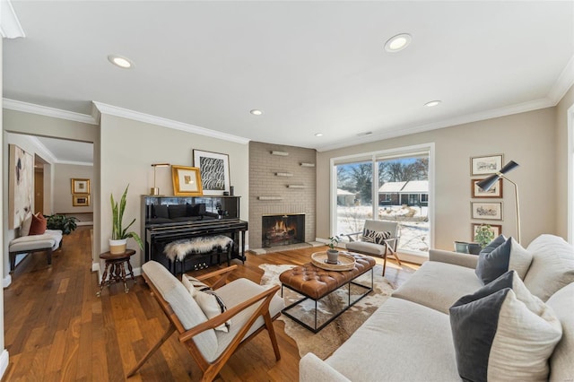 living area with recessed lighting, wood finished floors, baseboards, a brick fireplace, and crown molding