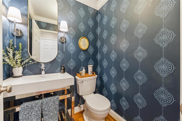 bathroom with wallpapered walls, baseboards, toilet, ornamental molding, and wood finished floors