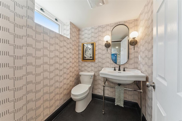 half bath featuring toilet, baseboards, a sink, and tile patterned floors