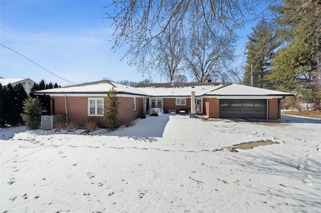 single story home with an attached garage, central air condition unit, and brick siding