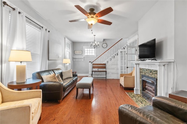 living room with hardwood / wood-style flooring, a tiled fireplace, and ceiling fan with notable chandelier