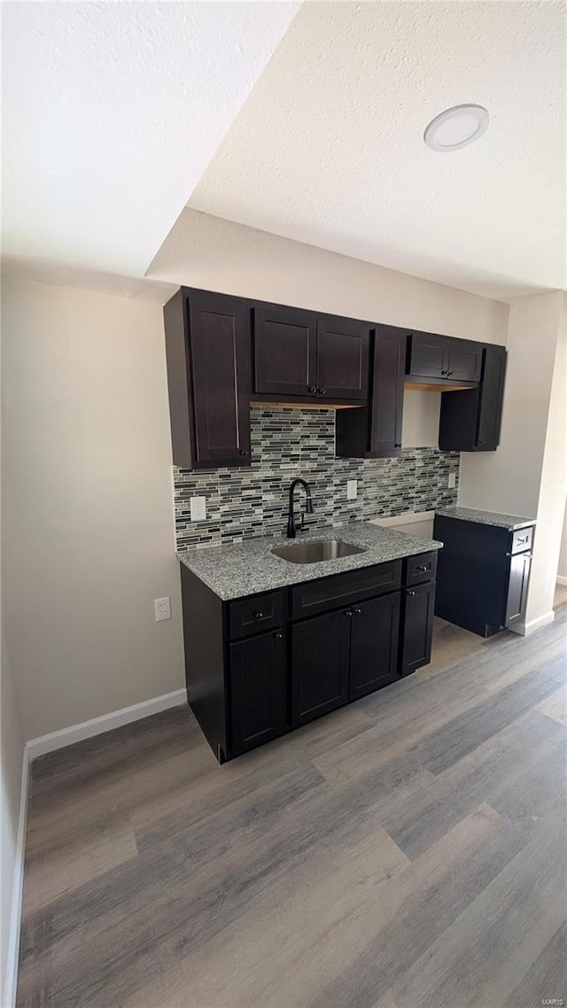 kitchen with tasteful backsplash, sink, light stone counters, and light wood-type flooring