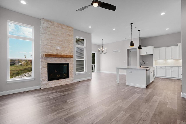 kitchen featuring a stone fireplace, sink, white cabinetry, hanging light fixtures, and an island with sink