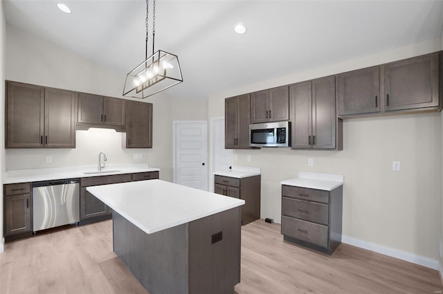 kitchen with sink, stainless steel appliances, light hardwood / wood-style floors, a kitchen island, and decorative light fixtures