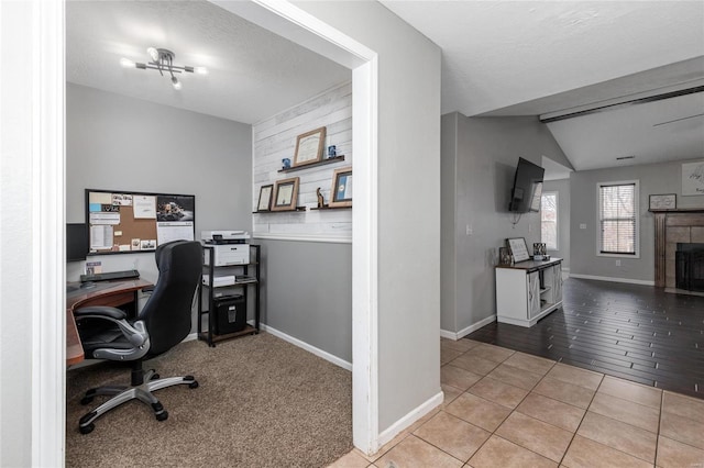 tiled office featuring vaulted ceiling, a tile fireplace, and a textured ceiling