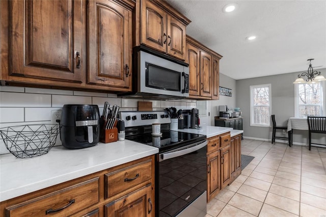 kitchen featuring tasteful backsplash, hanging light fixtures, light tile patterned floors, stainless steel appliances, and an inviting chandelier