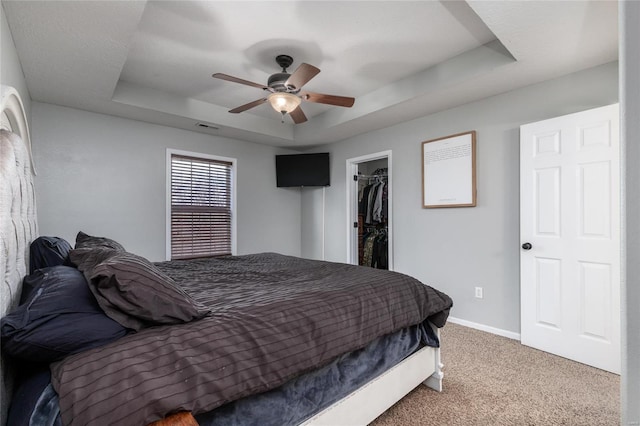 carpeted bedroom featuring a raised ceiling, a spacious closet, ceiling fan, and a closet