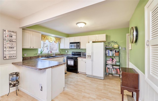 kitchen featuring black range with gas cooktop, white cabinetry, white refrigerator with ice dispenser, and kitchen peninsula