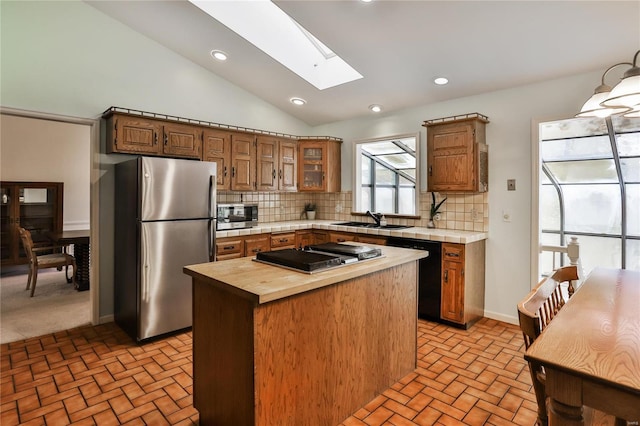 kitchen featuring sink, tasteful backsplash, a kitchen island, stainless steel appliances, and vaulted ceiling with skylight