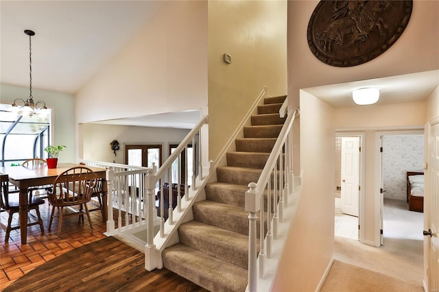 staircase with an inviting chandelier, plenty of natural light, and high vaulted ceiling