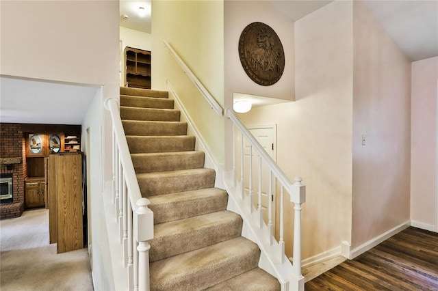 staircase with wood-type flooring and a brick fireplace