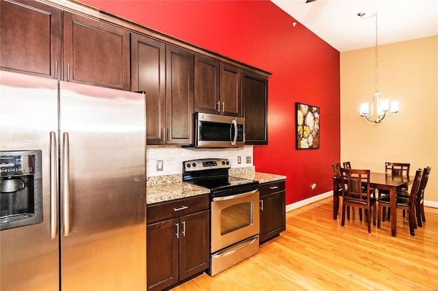 kitchen with an inviting chandelier, stainless steel appliances, dark brown cabinetry, light stone countertops, and decorative light fixtures