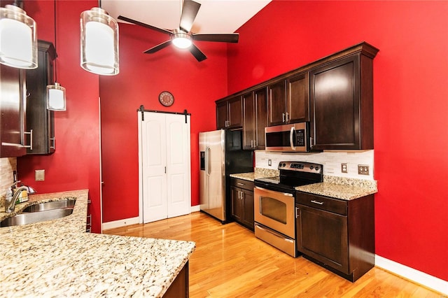 kitchen featuring sink, appliances with stainless steel finishes, tasteful backsplash, a barn door, and light wood-type flooring