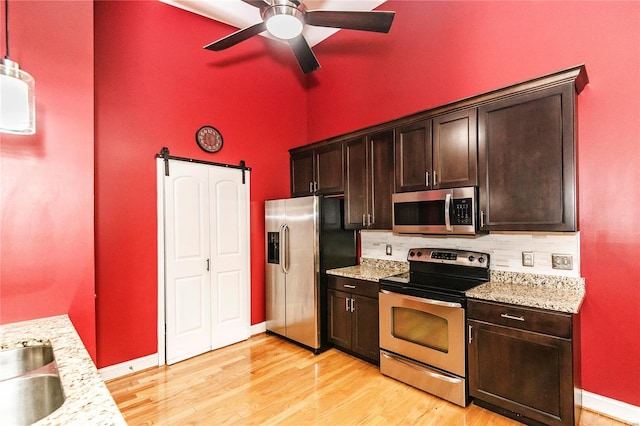 kitchen featuring dark brown cabinetry, light stone counters, a barn door, and appliances with stainless steel finishes