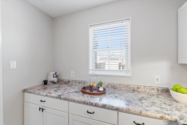 kitchen featuring light stone countertops, a textured ceiling, and white cabinets