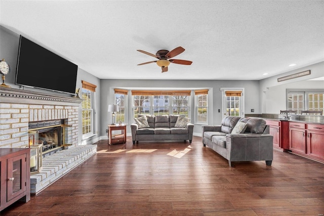 living room featuring ceiling fan, a brick fireplace, dark hardwood / wood-style floors, and a textured ceiling