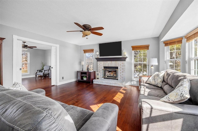 living room with ceiling fan, dark hardwood / wood-style flooring, a brick fireplace, and a textured ceiling