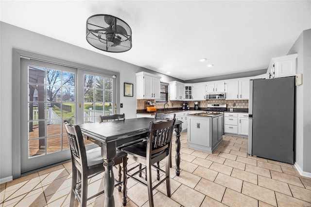 kitchen with sink, appliances with stainless steel finishes, white cabinetry, backsplash, and a kitchen island