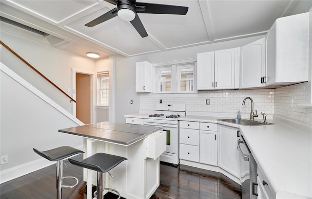 kitchen featuring sink, a breakfast bar, white range with gas stovetop, white cabinets, and a kitchen island