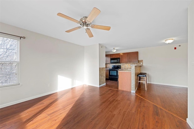 unfurnished living room with ceiling fan, baseboards, and wood finished floors