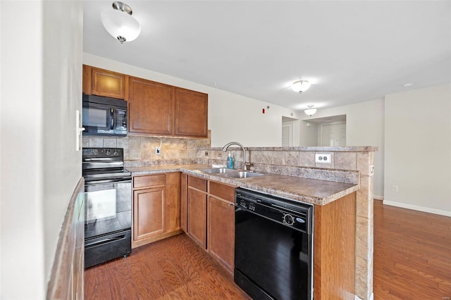 kitchen featuring tasteful backsplash, wood finished floors, a peninsula, black appliances, and a sink