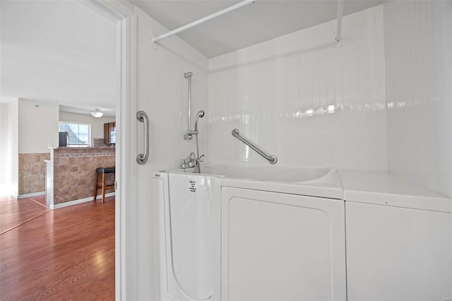 bathroom featuring washer / dryer, a washtub, a wainscoted wall, and wood finished floors