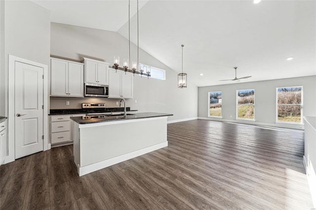 kitchen with dark countertops, an island with sink, open floor plan, stainless steel appliances, and white cabinetry