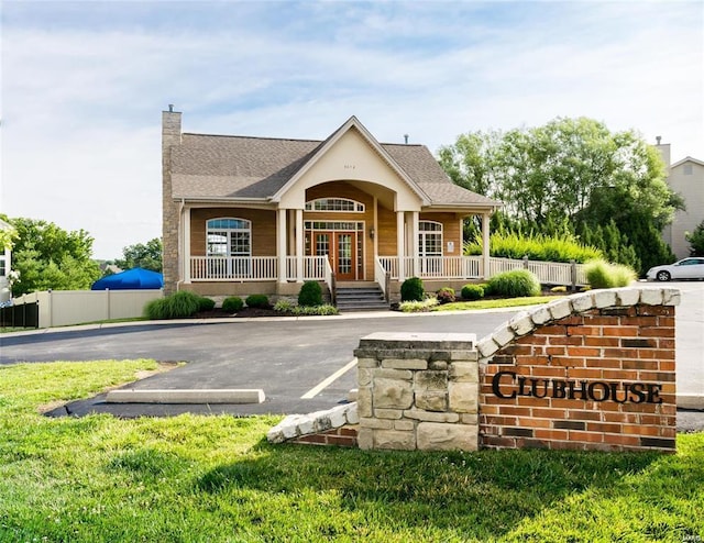 view of front of house with a shingled roof, a chimney, fence, uncovered parking, and a porch