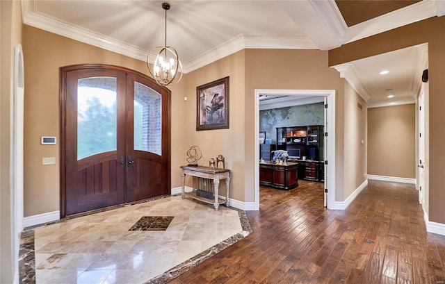 foyer entrance featuring french doors, wood-type flooring, crown molding, and a notable chandelier