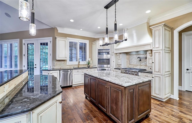 kitchen with hanging light fixtures, dark stone countertops, appliances with stainless steel finishes, dark hardwood / wood-style floors, and a kitchen island