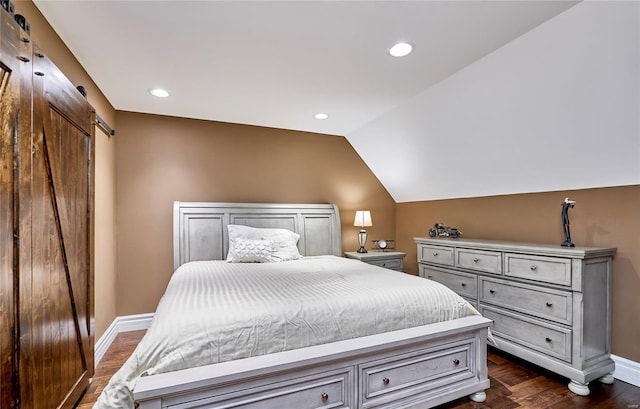 bedroom featuring dark wood-type flooring, a barn door, and vaulted ceiling