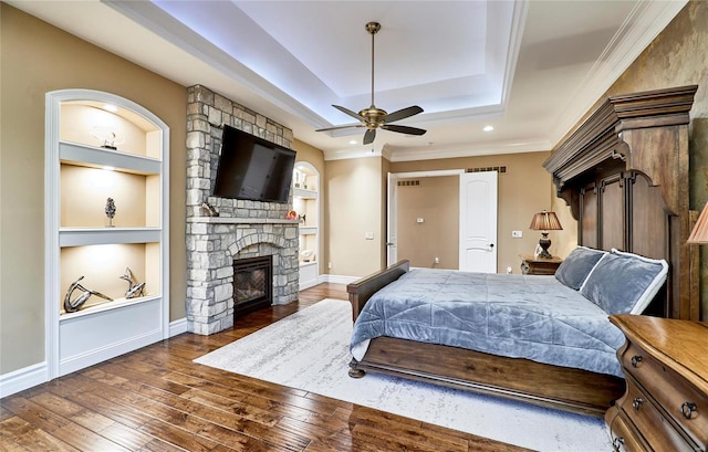 bedroom featuring ornamental molding, dark wood-type flooring, a fireplace, and a tray ceiling