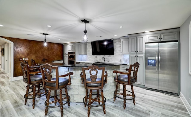 bar with tasteful backsplash, decorative light fixtures, appliances with stainless steel finishes, gray cabinets, and light hardwood / wood-style floors