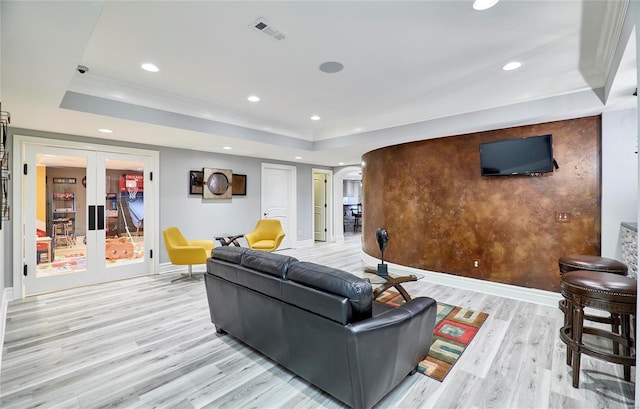 living room featuring crown molding, light wood-type flooring, a raised ceiling, and french doors