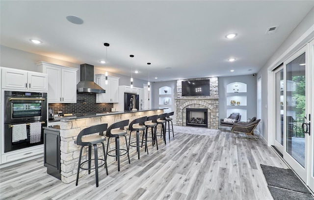 kitchen with pendant lighting, wall chimney range hood, a breakfast bar, double oven, and white cabinets