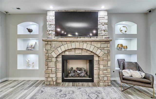 interior details featuring hardwood / wood-style floors, a stone fireplace, and built in shelves