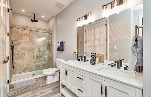 bathroom with a tile shower, vanity, wood-type flooring, and toilet