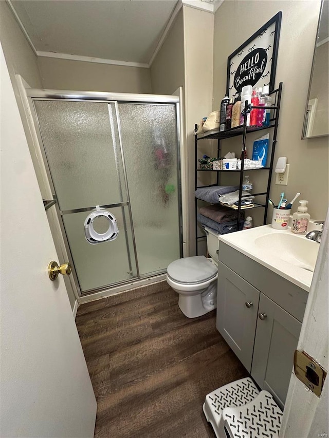 bathroom with wood-type flooring, ornamental molding, vanity, an enclosed shower, and toilet